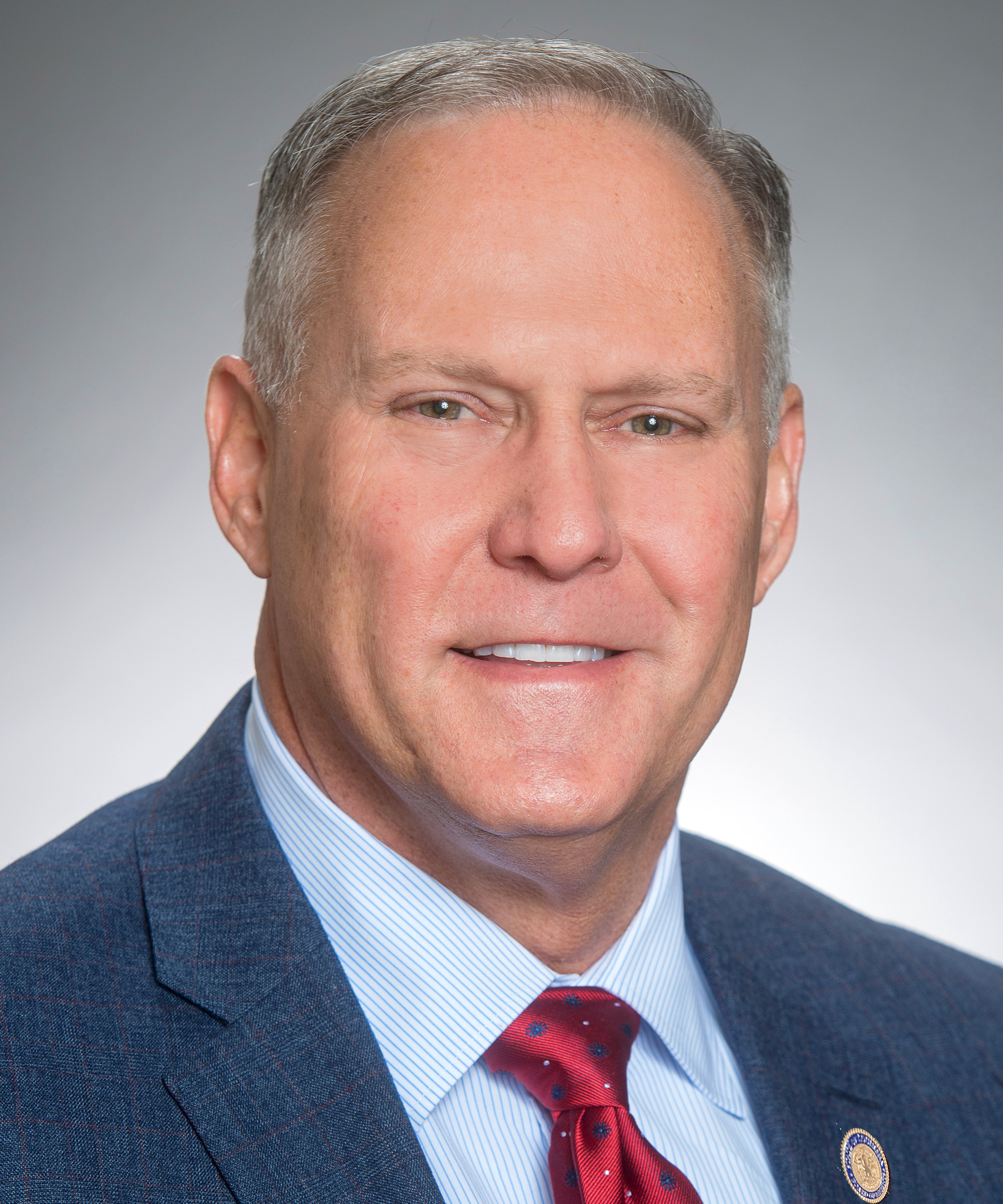 White male in dark blue suit, blue shirt, and red tie