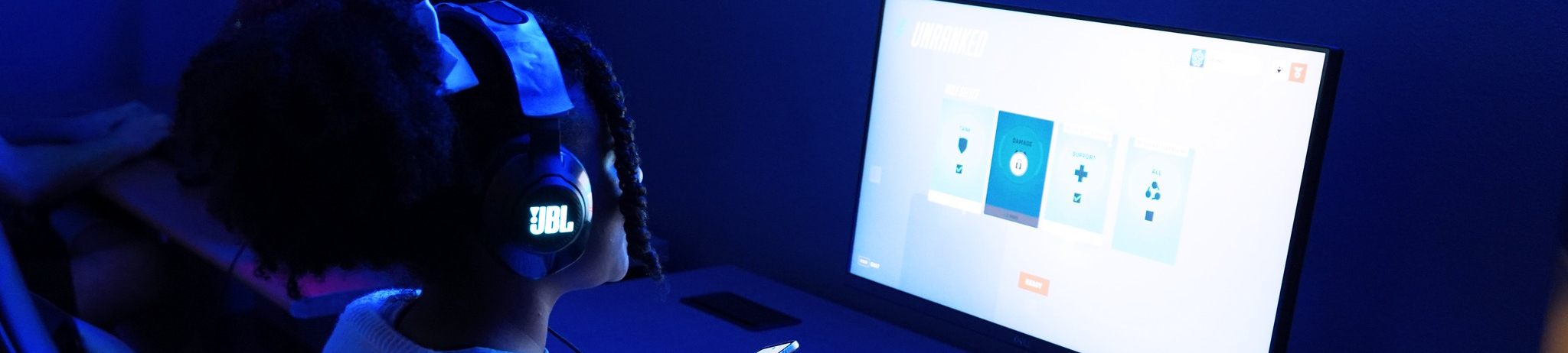 Girl with hair up and headphones on viewing computer screen in dark lit room